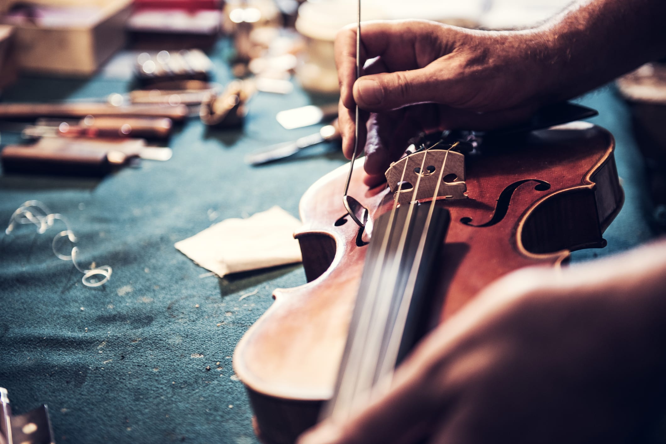 Portrait of senior entrepreneur working in his instrument repair shop, taking care of violins and other music instruments. Experienced senior is using his skills to repair instruments